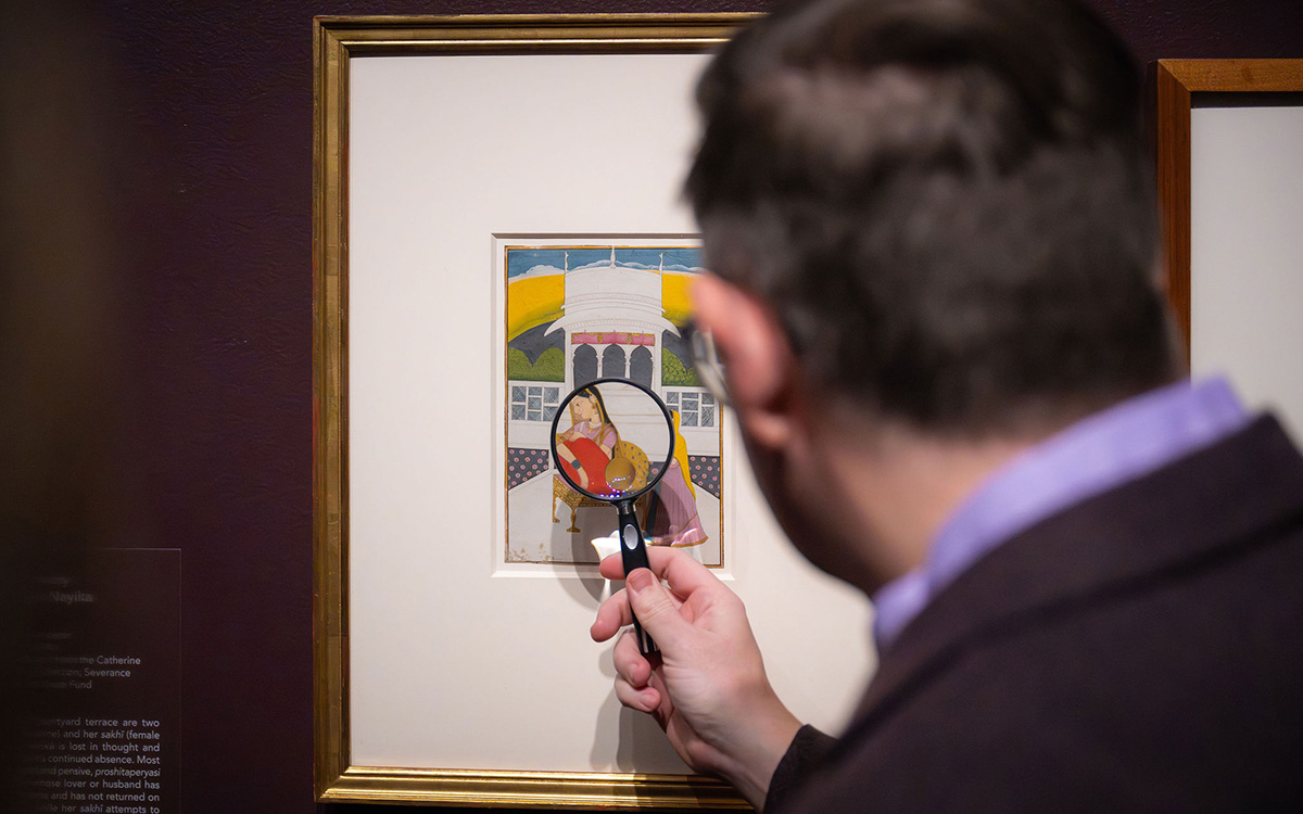 A man examines the details of a small painting using a magnifying glass.
