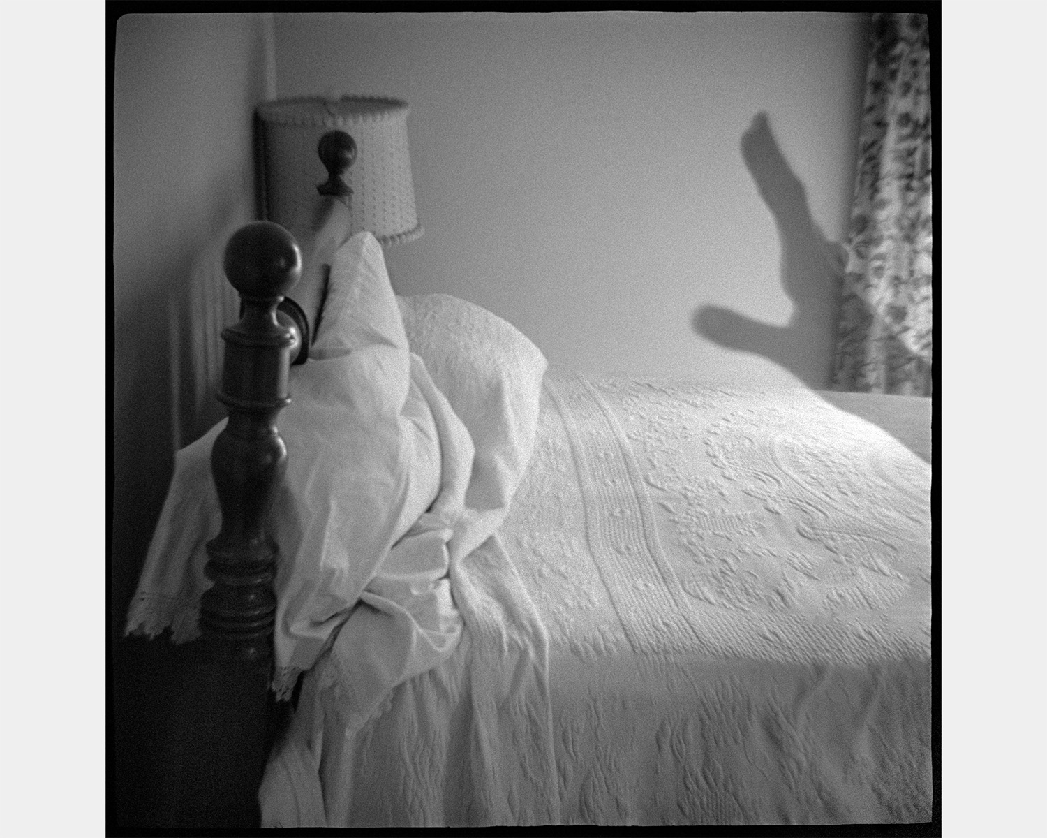 A black and white photo of the shadow of a hand over a made bed