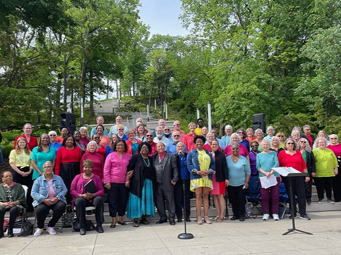 A large group of colorfully dressed people stand on an outdoor stairway that winds up a wooded hillside.