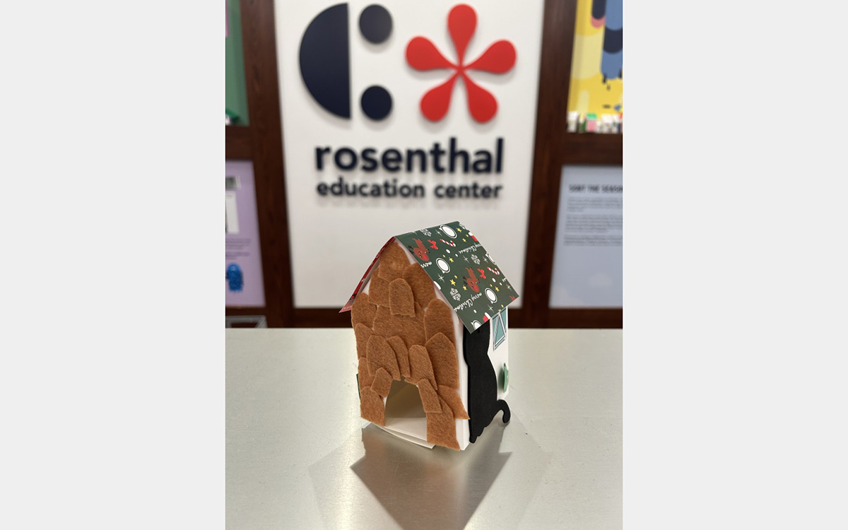 Small colorful model of a house on a tabletop with a "rosenthal education center" sign on wall in background.