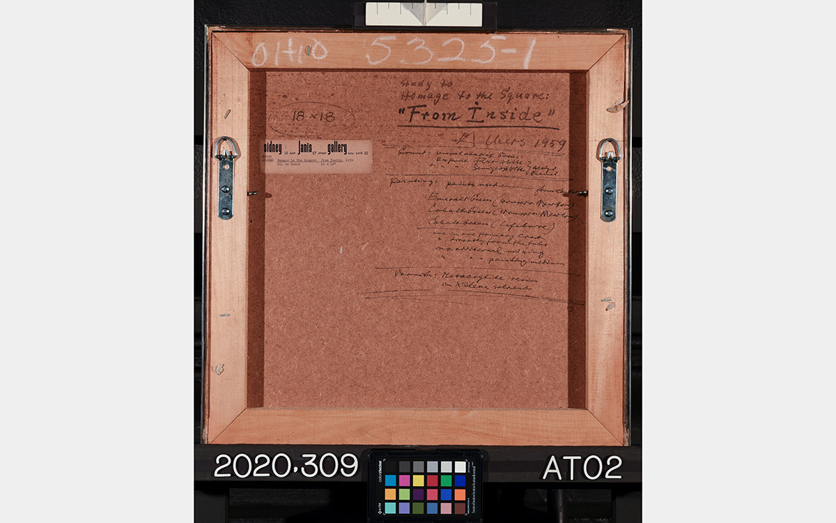 Back of a square painting showing a wood frame surrounding a wood board with notes written on it, and a color grid below and ruler above.